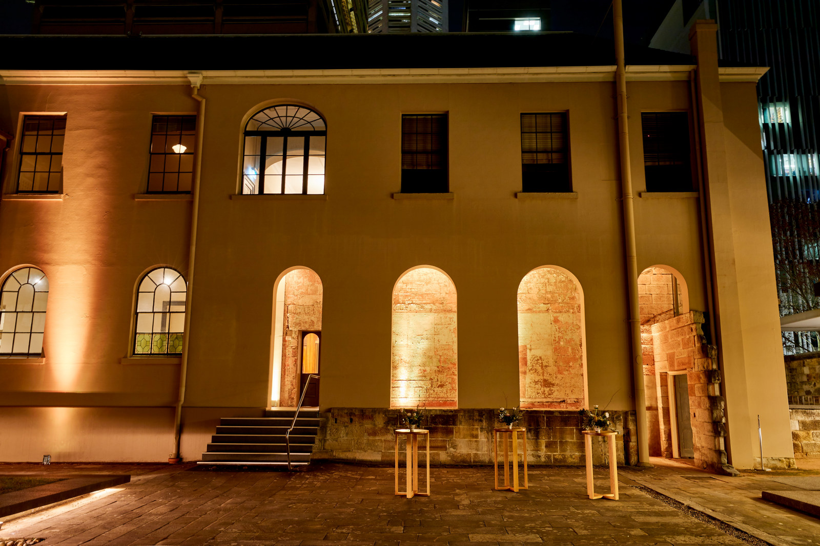 Rear of the Mint building lit up and tables in the Courtyard