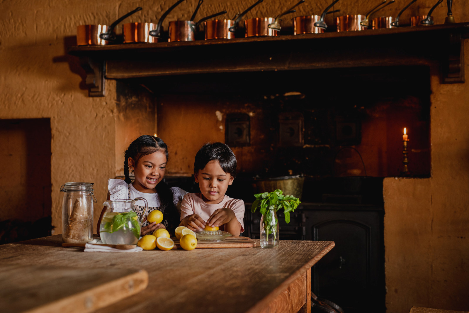 Two kids juicing lemons at a big wooden table in the kitchen at Elizabeth Farm.