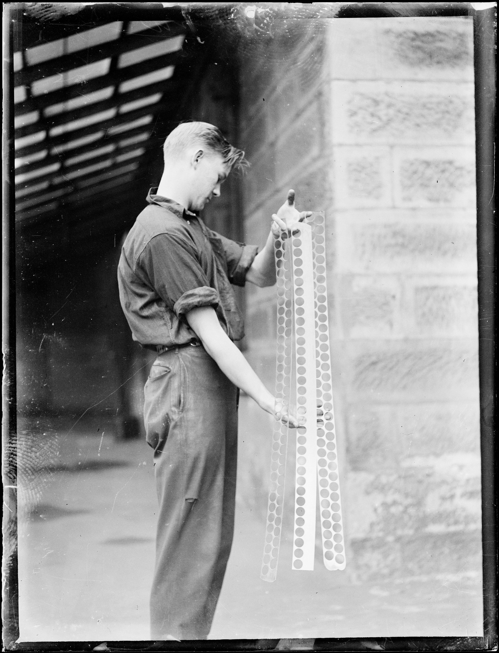 Black and white photo of a young man holding long silver moulds used for casting coins