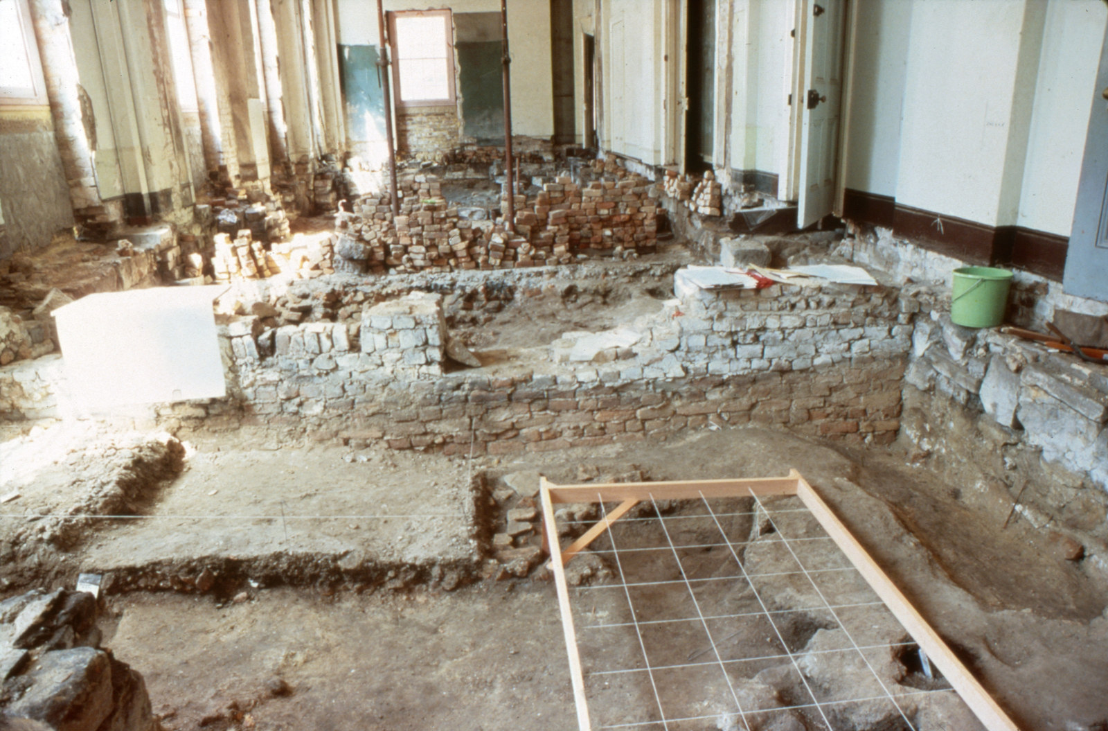 North-east ground floor room of Hyde Park Barracks during excavation, looking east, 1980-81. An archaeological grid is overlaid on a rat burrow in the foreground.