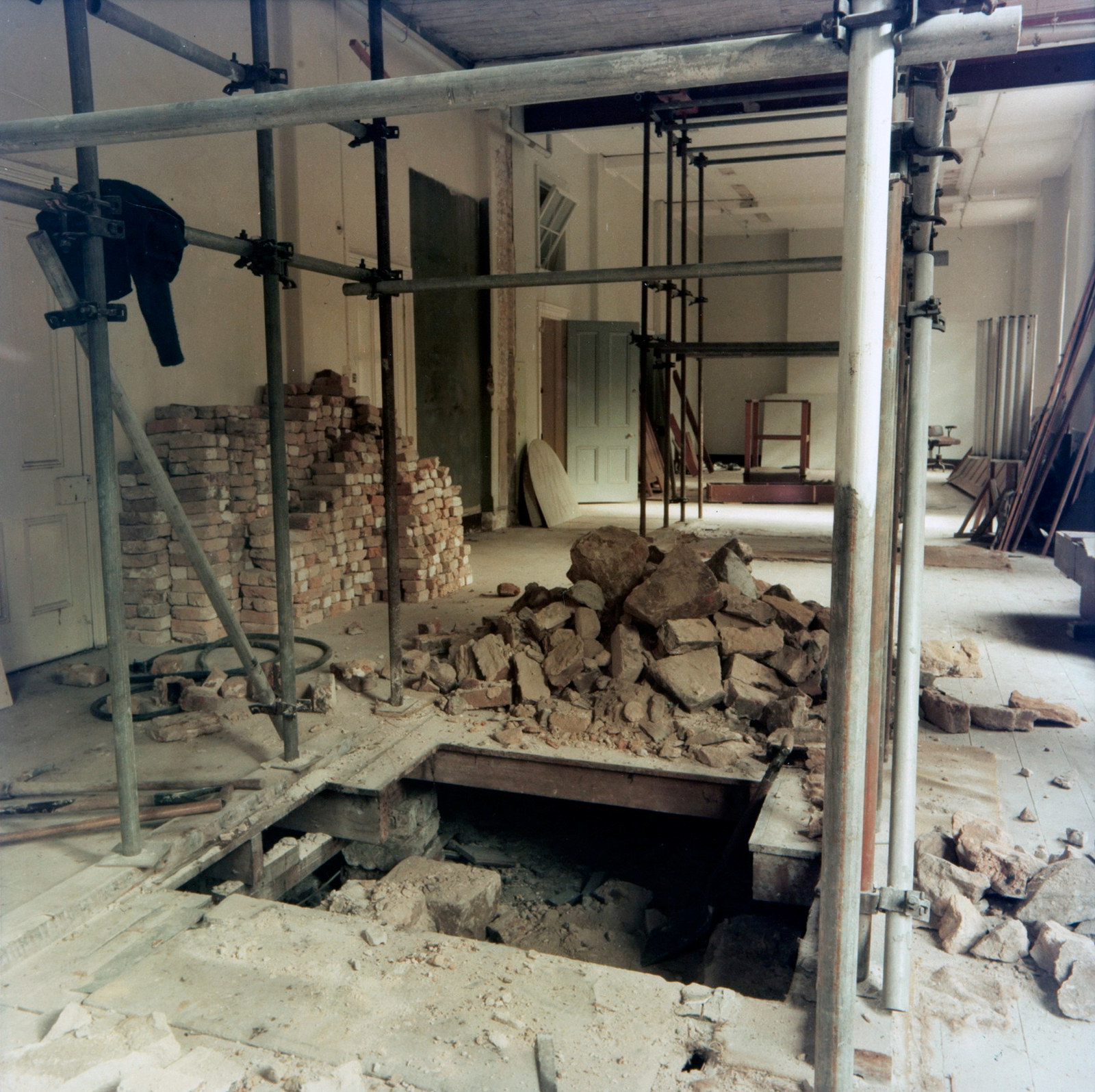 Long room with internal scaffolding, a section of floor removed and a pile of bricks stacked neatly to one side.