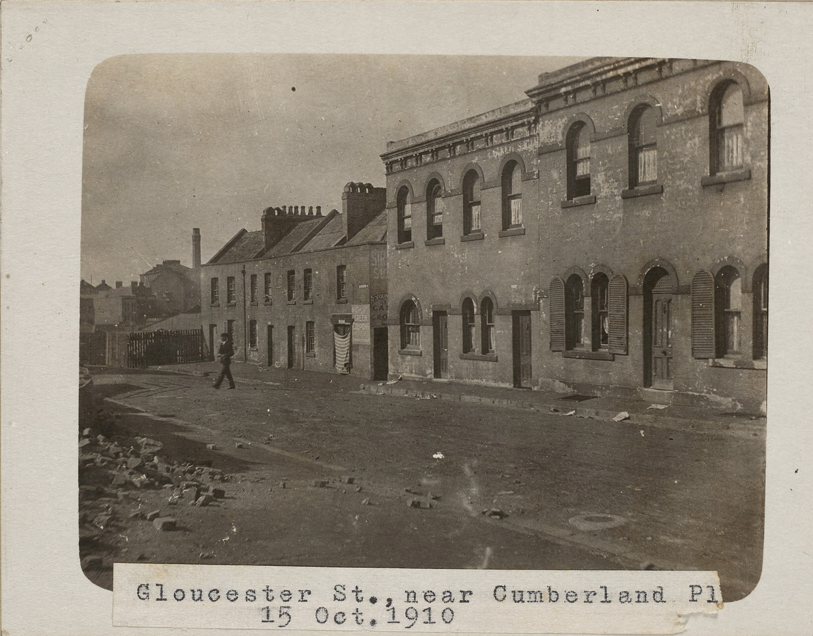 Black and white photograph of Gloucester Street showing Susannah Place terraces; The Youngein grocer shop has a stripped curtain hanging over the window.