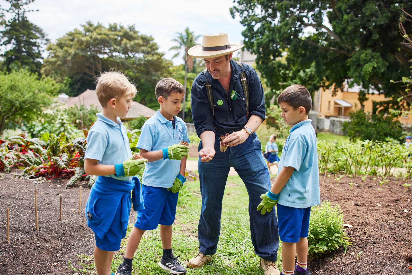 CPD Damien Egan showing seeds to students holding pots and wearing gardening gloves in the kitchen garden.