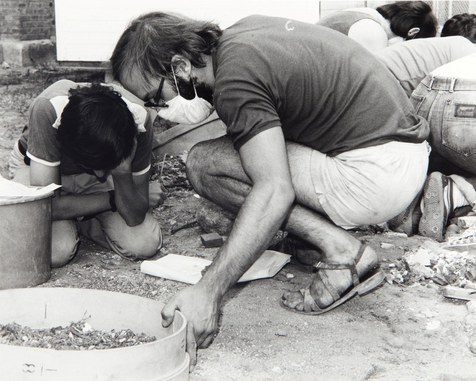 Two men crouching over sieve