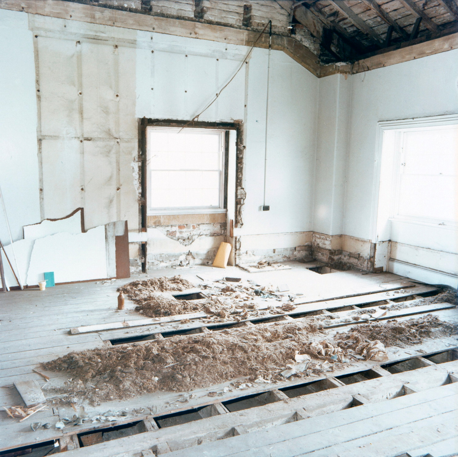 Room with wooden floorboards lifted in centre, with piles of extracted materials.