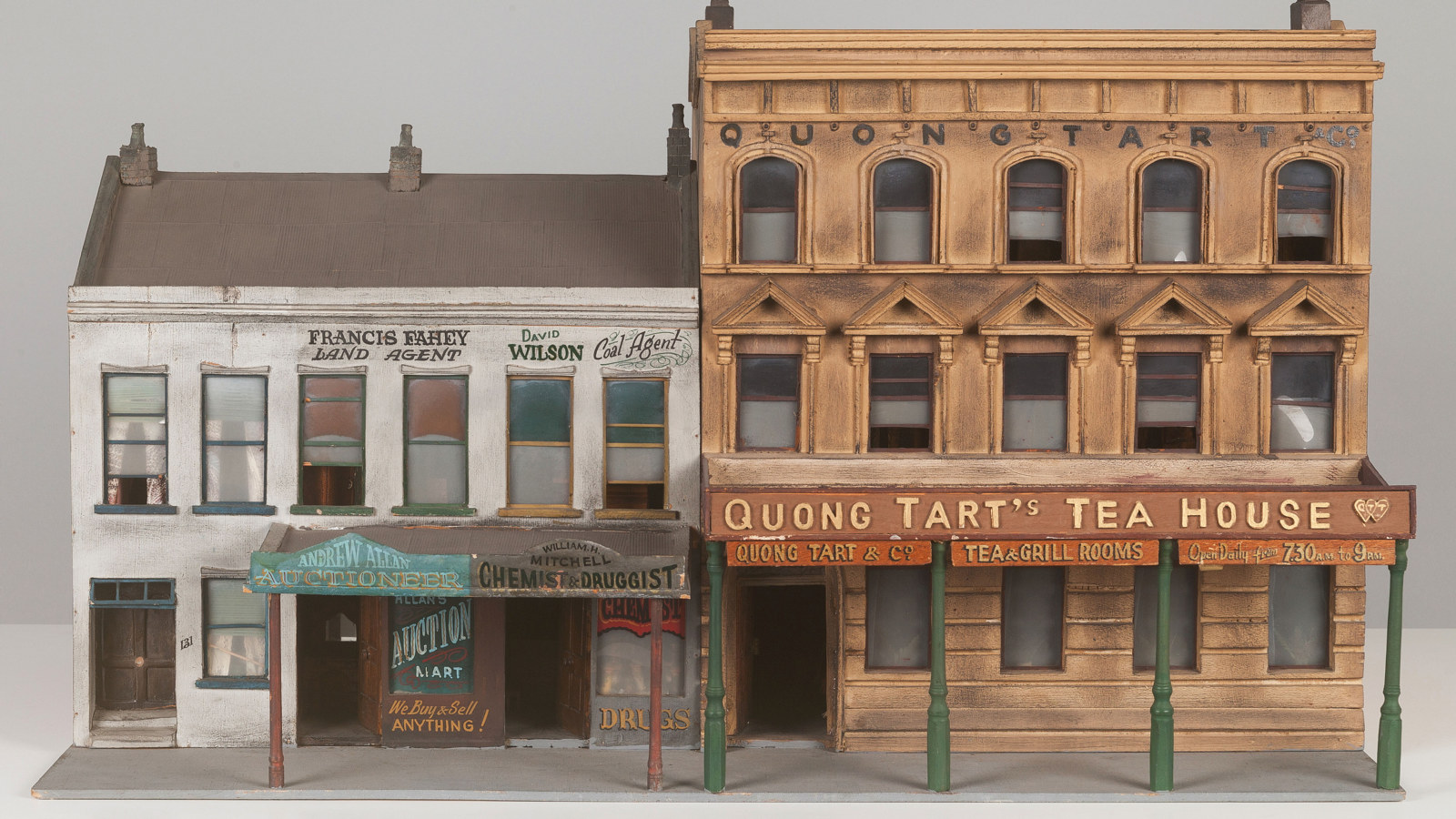 Architectural model of 2 adjoining buildings with verandahs facing a street. Awnings on the verandahs contain colourful signage and the names of businesses are written on the walls of the buildings.