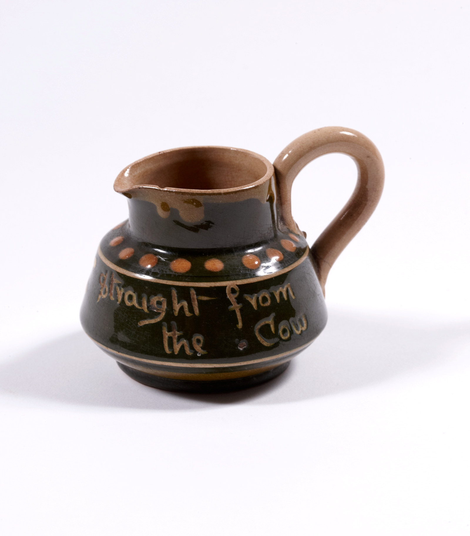 Torquay motto ware miniature cream jug made from glazed earthenware, 'Straight from the Cow' inscribed on one side