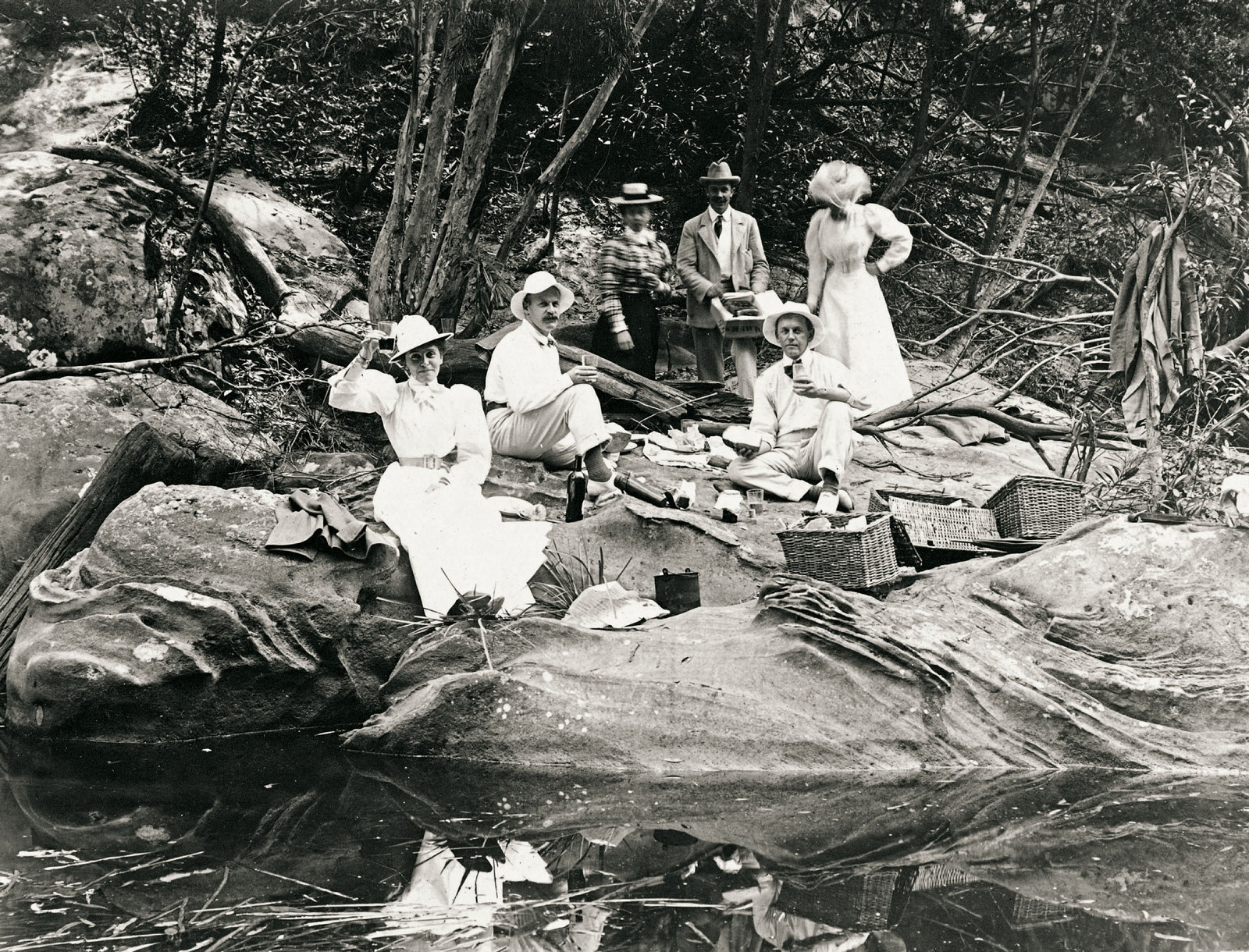 Group of people sit on rocks beside a quite stream after a picnic