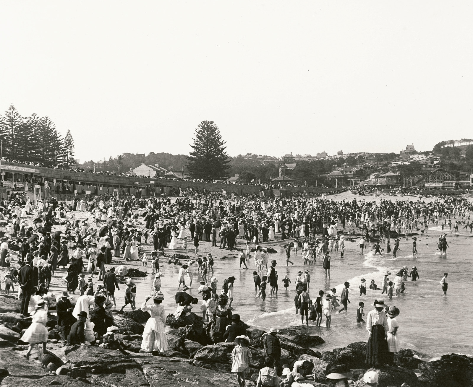 Crowds cover the rocks and sand at Coogee Beach on a hot day.